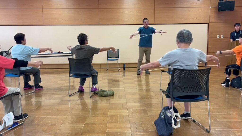 紐を手に、座ったまま腕の動きを確かめる参加者の皆さん